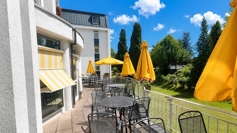 Sonnenterrasse der Falkenstein-Klinik mit Bistrostühlen, Tischen, Sonnenschirmen und Ausblick